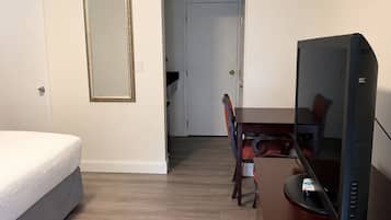 A hotel room with a bed, a desk with a computer, a chair, and a door leading to another room.