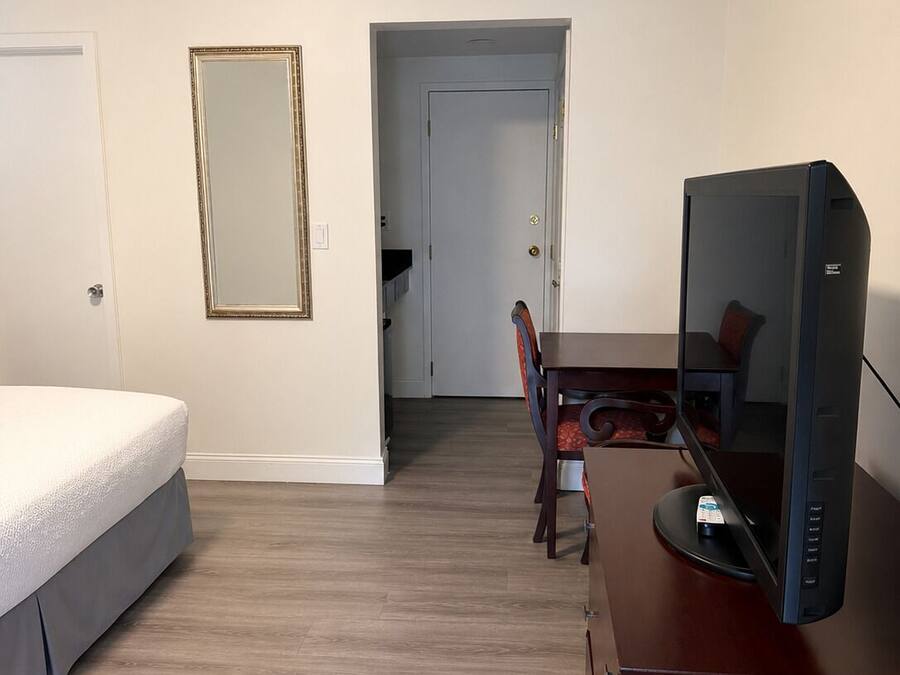A hotel room with a bed, a desk with a computer, a chair, and a door leading to another room.