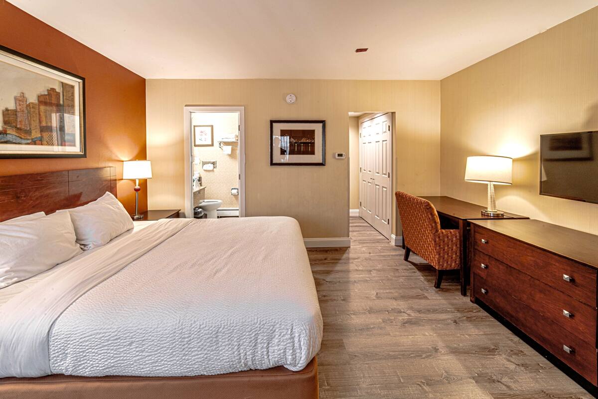 Une chambre d’hôtel avec un grand lit, un bureau avec une chaise, une télévision et une porte donnant sur une salle de bain.