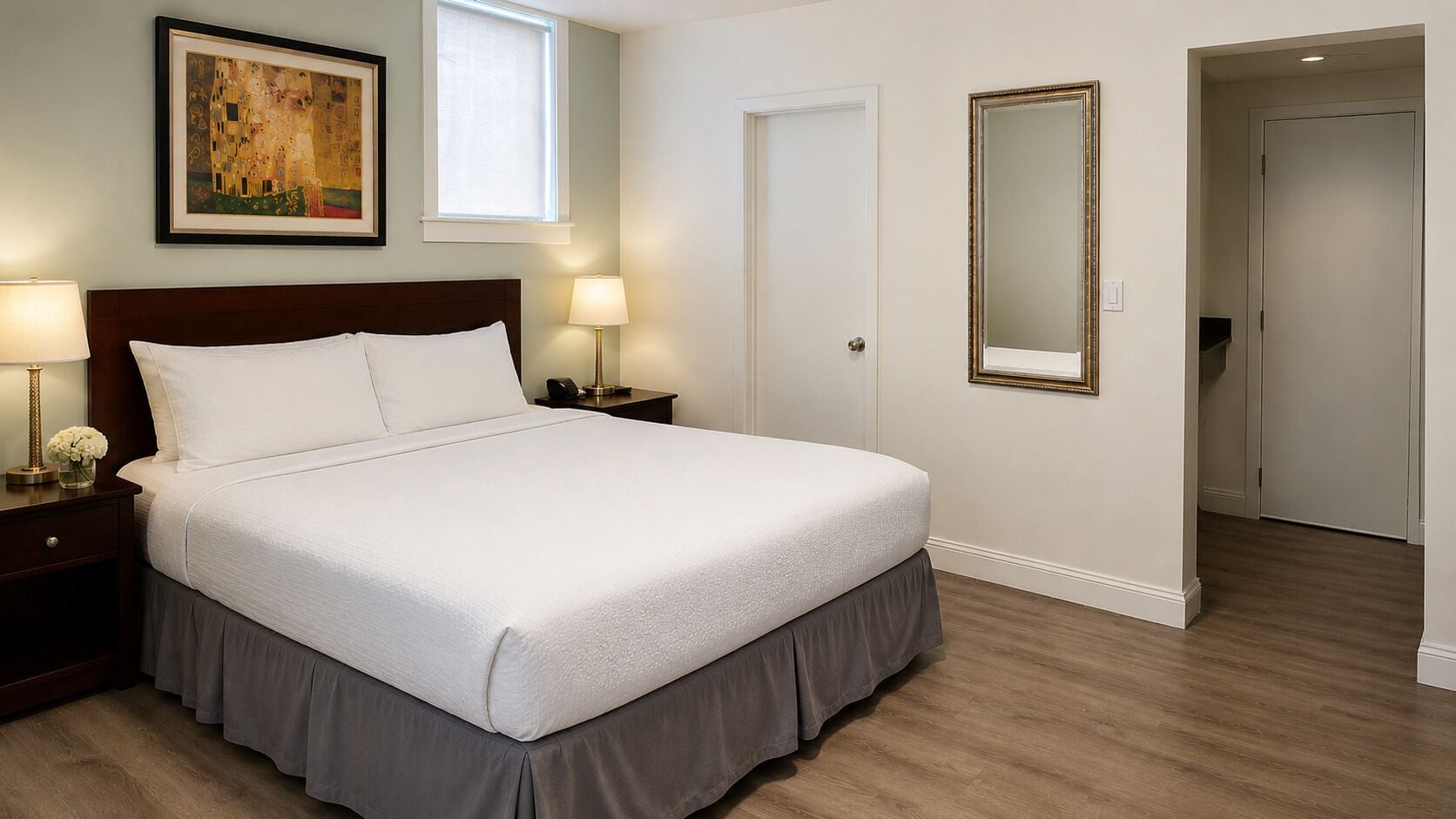 A hotel room with a large bed, bedside lamps, a framed painting, and a mirror.