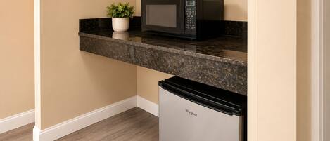A kitchen with a microwave, a small refrigerator, and a potted plant on the countertop.