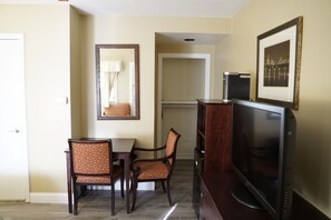 A hotel room with a dining area featuring a table and two chairs, a television on a stand, a framed picture on the wall, and a door. - The Boston Hotel (Boston)