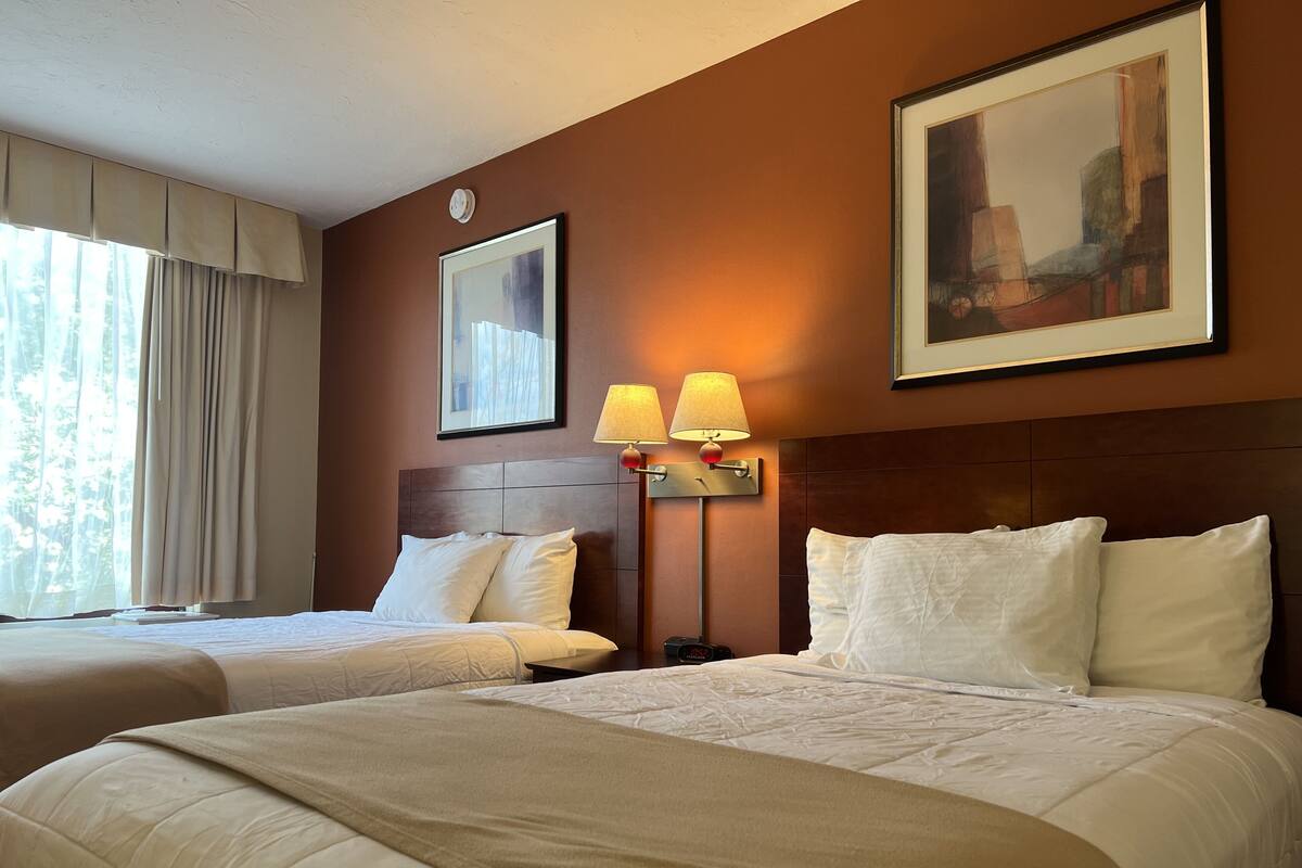 Une chambre d’hôtel avec deux lits, un grand tableau et une lampe fixée au mur.