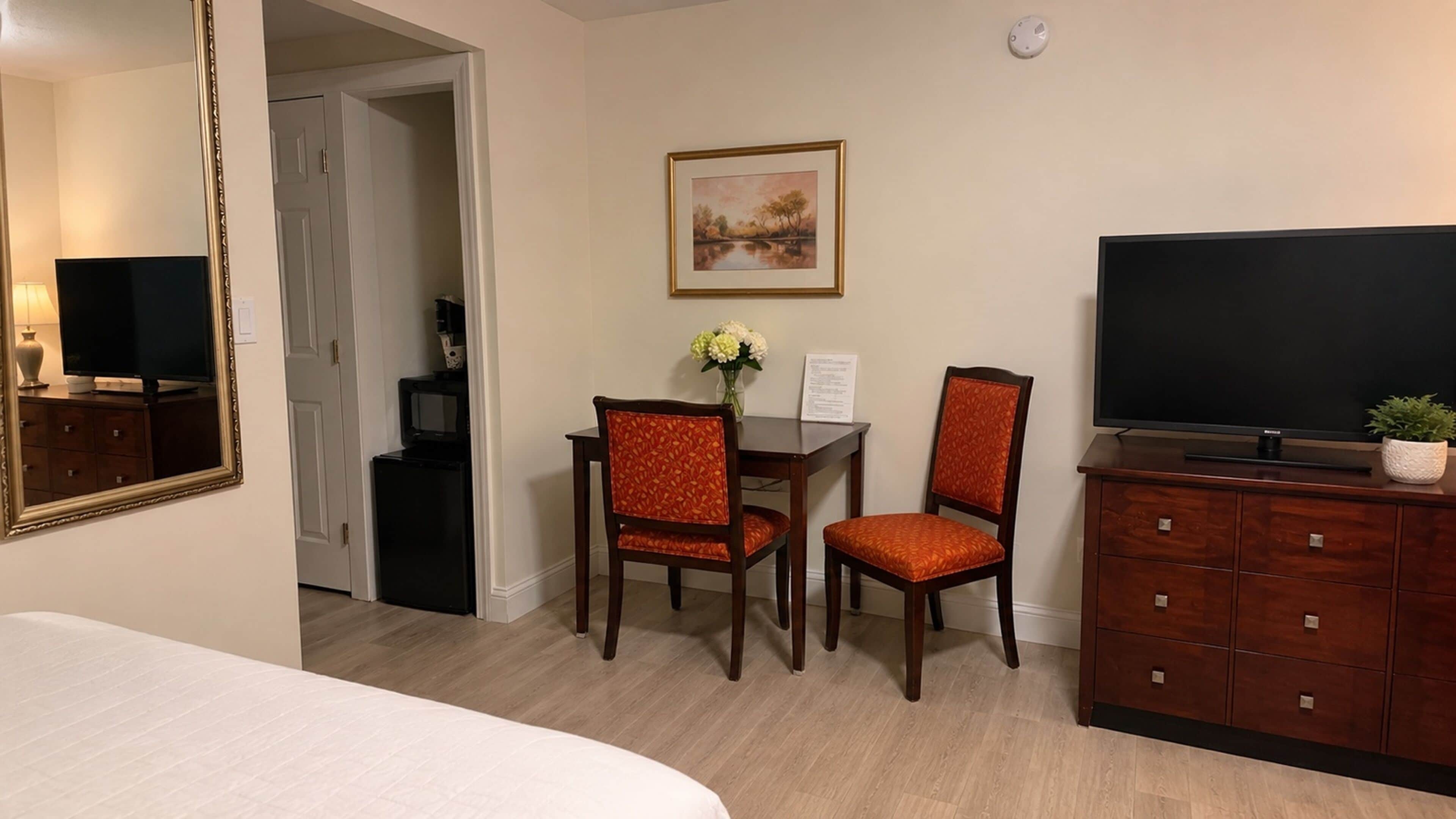Habitación de hotel con una cama, un televisor, un escritorio con dos sillas, un aparador y un cuadro en la pared.