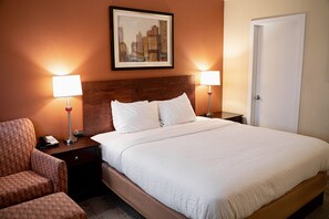 A hotel room with a large bed, two bedside lamps, a framed cityscape picture on the wall, a door, and a chair. - Hotel Boston (Boston)