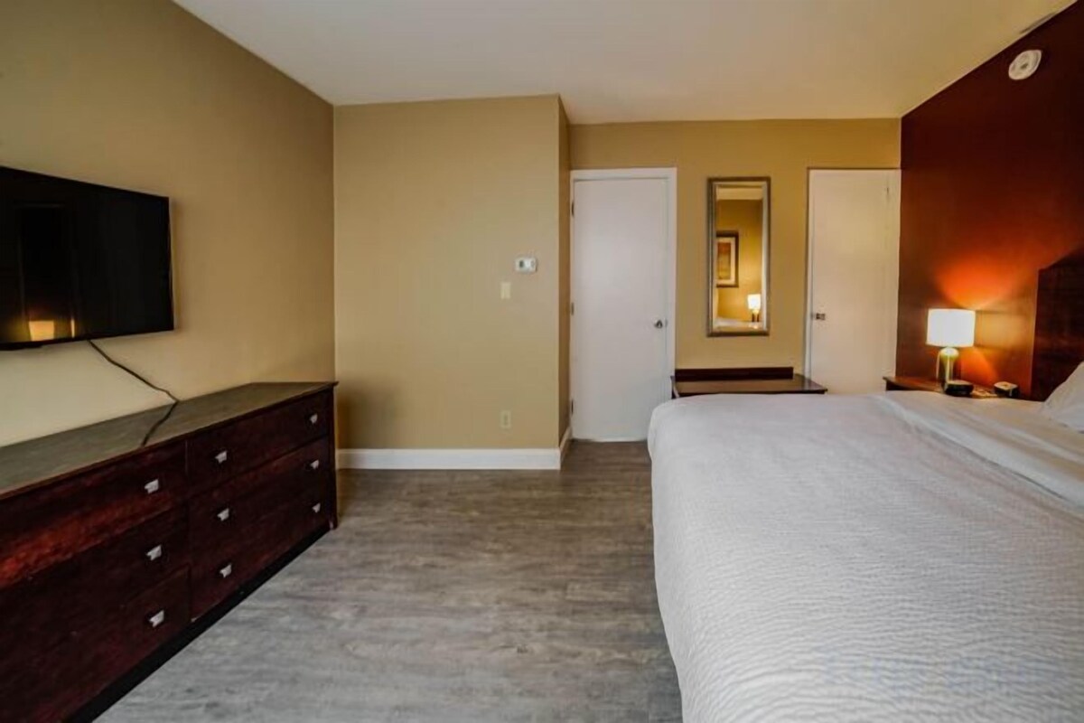 A hotel room with a bed, a dresser, a television, a door, and a mirror.