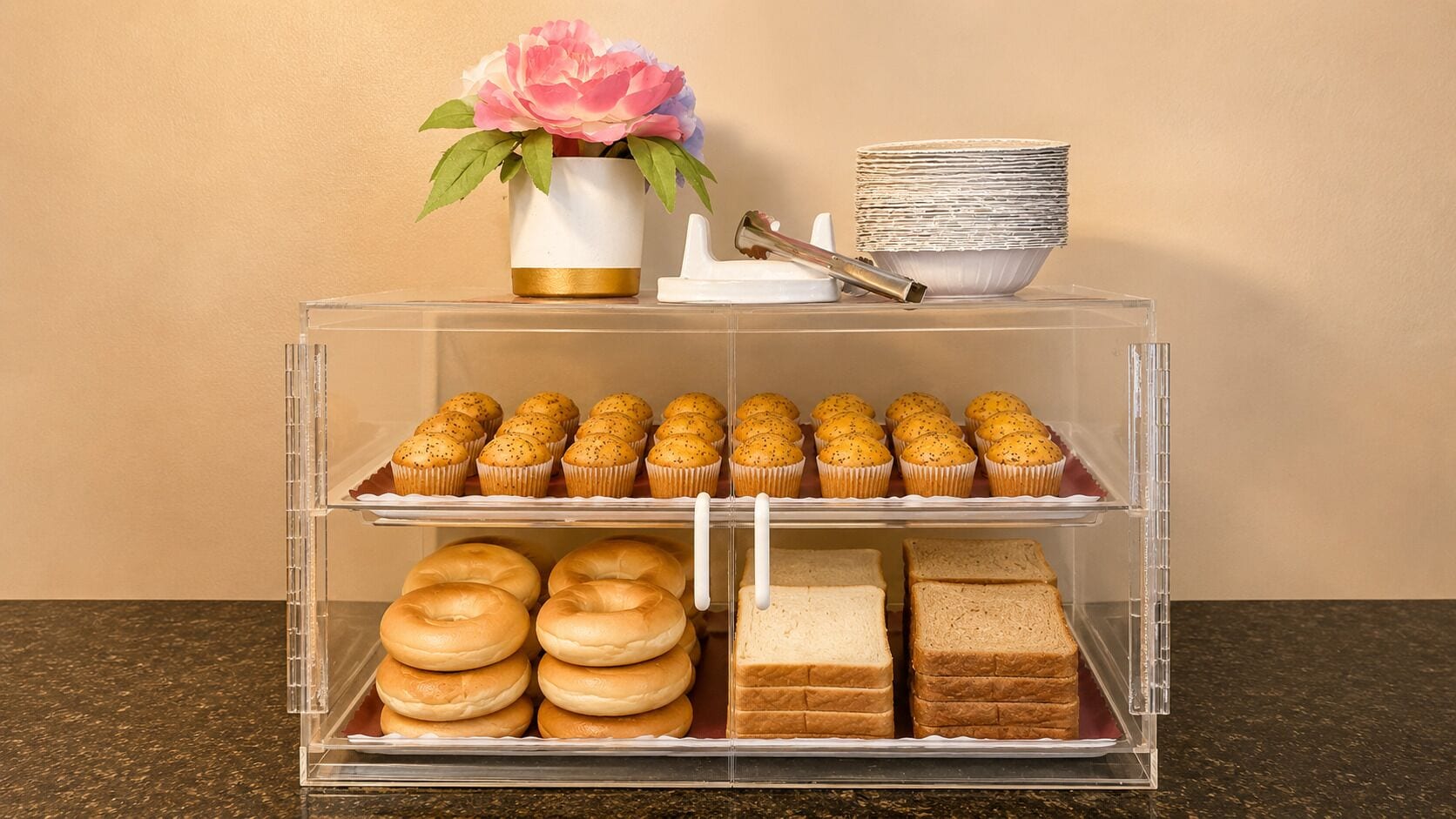 Vitrine transparente com pastéis, sanduíches e um vaso de flores.