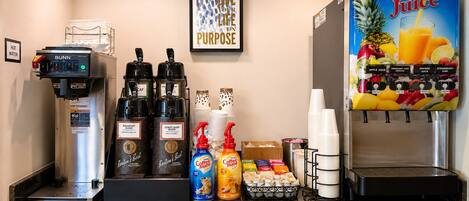 A coffee station with a coffee machine, two coffee dispensers, a juice dispenser, and various coffee and creamer options.