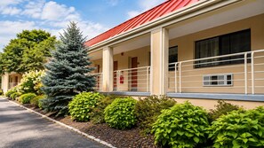 Un motel avec un toit rouge, des murs extérieurs de couleur beige et une véranda couverte dotée d’une balustrade blanche.