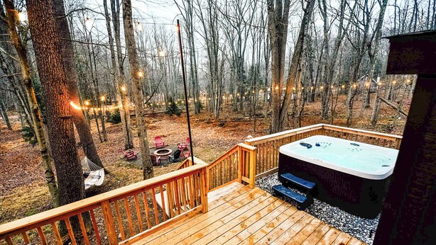Een houten terras met een jacuzzi, omgeven door bomen en sfeerverlichting.