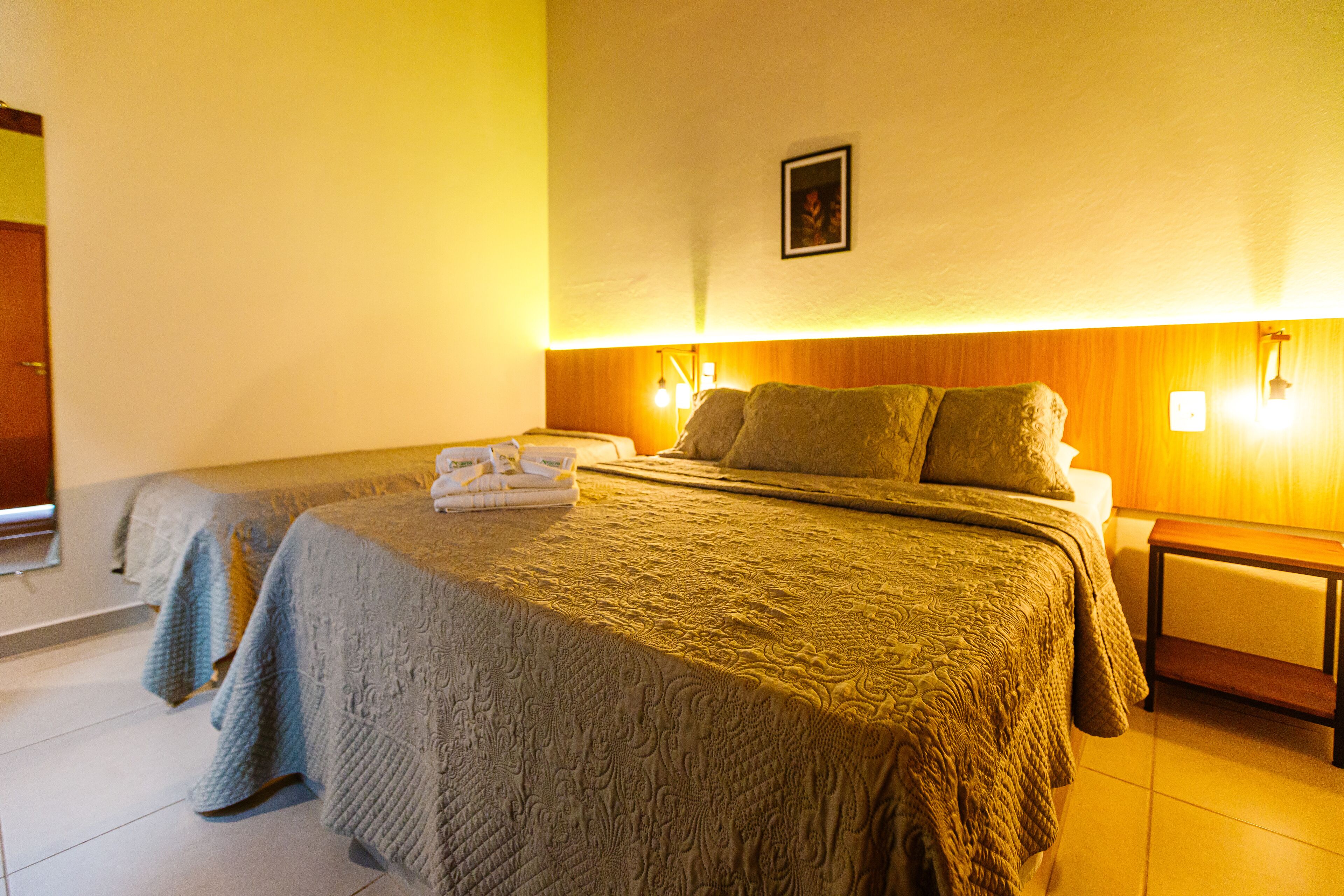 Een hotelkamer met een groot bed, een kleiner bed en een nachtkastje met een lamp.