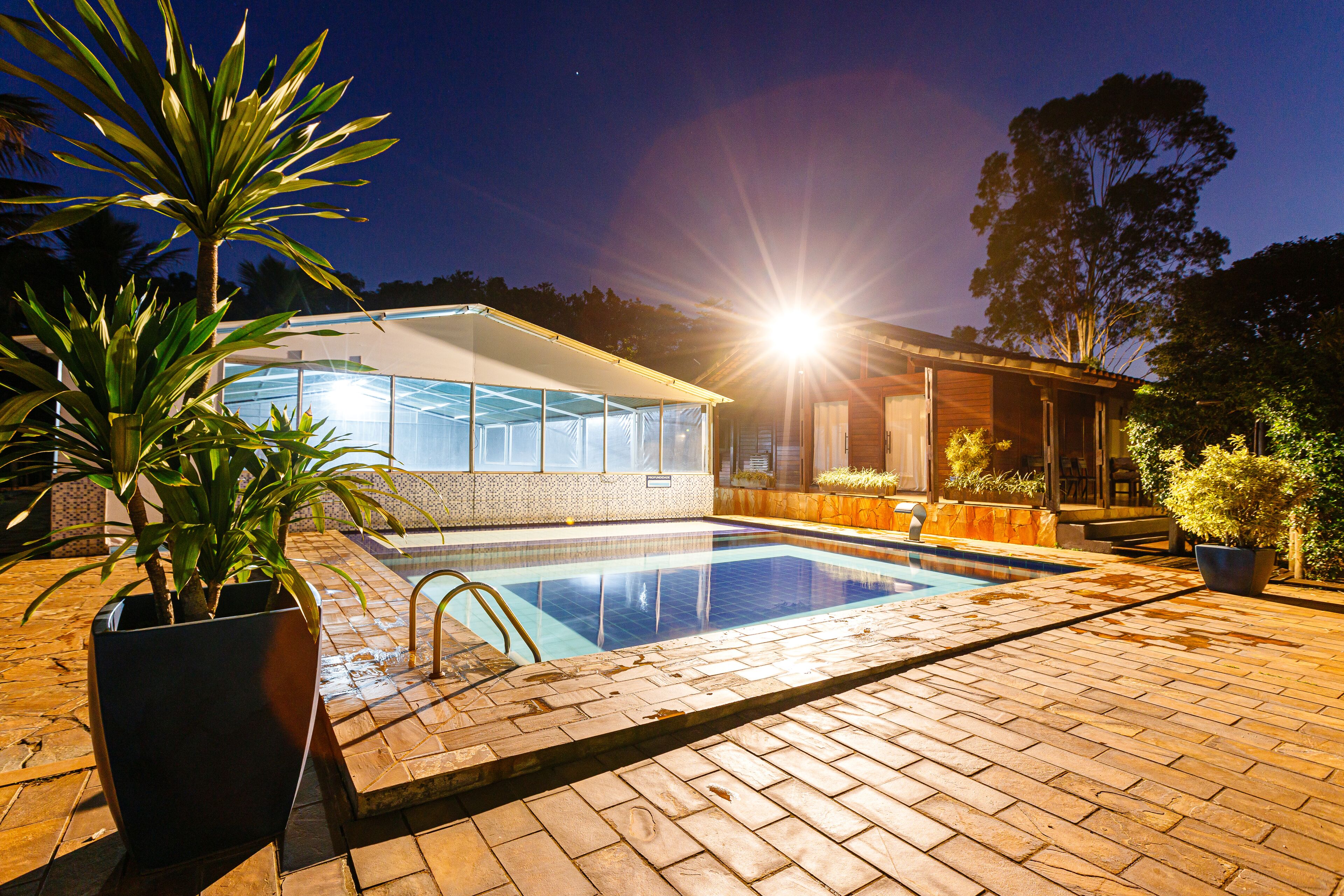 A swimming pool with a glass enclosure, surrounded by a brick patio and potted plants.