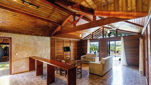 Une pièce spacieuse avec un mur en pierre, des poutres en bois au plafond, un banc en bois, un canapé et un téléviseur fixé au mur.