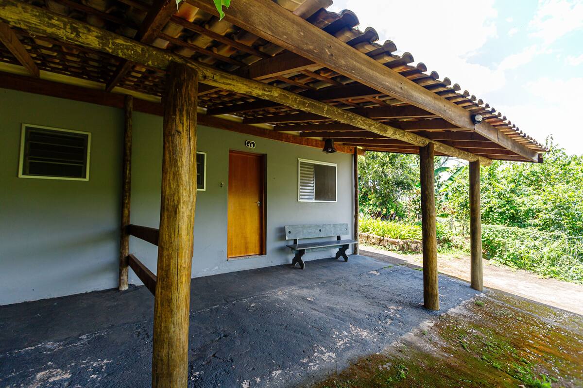 Un espacio al aire libre cubierto con una banca, pilares de madera y la entrada de un edificio.