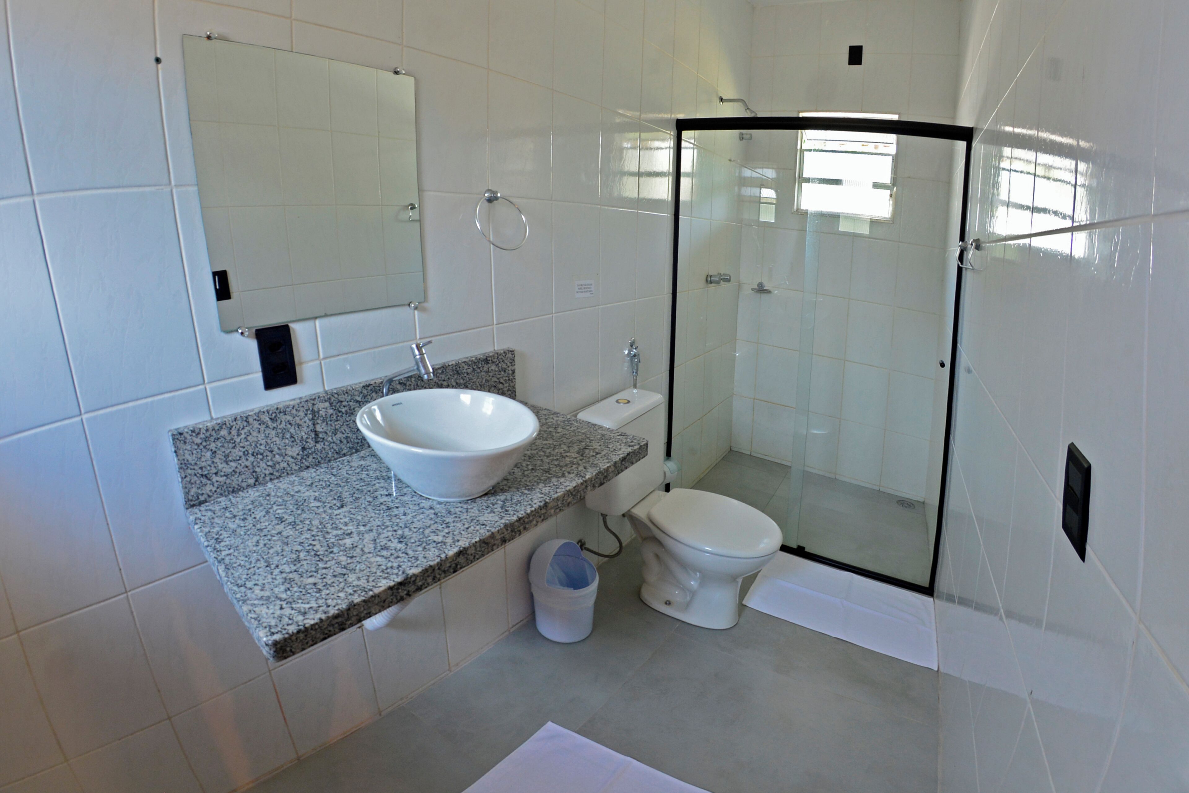 Un baño moderno con encimera de granito, lavamanos blanco, inodoro y ducha con mampara de vidrio.