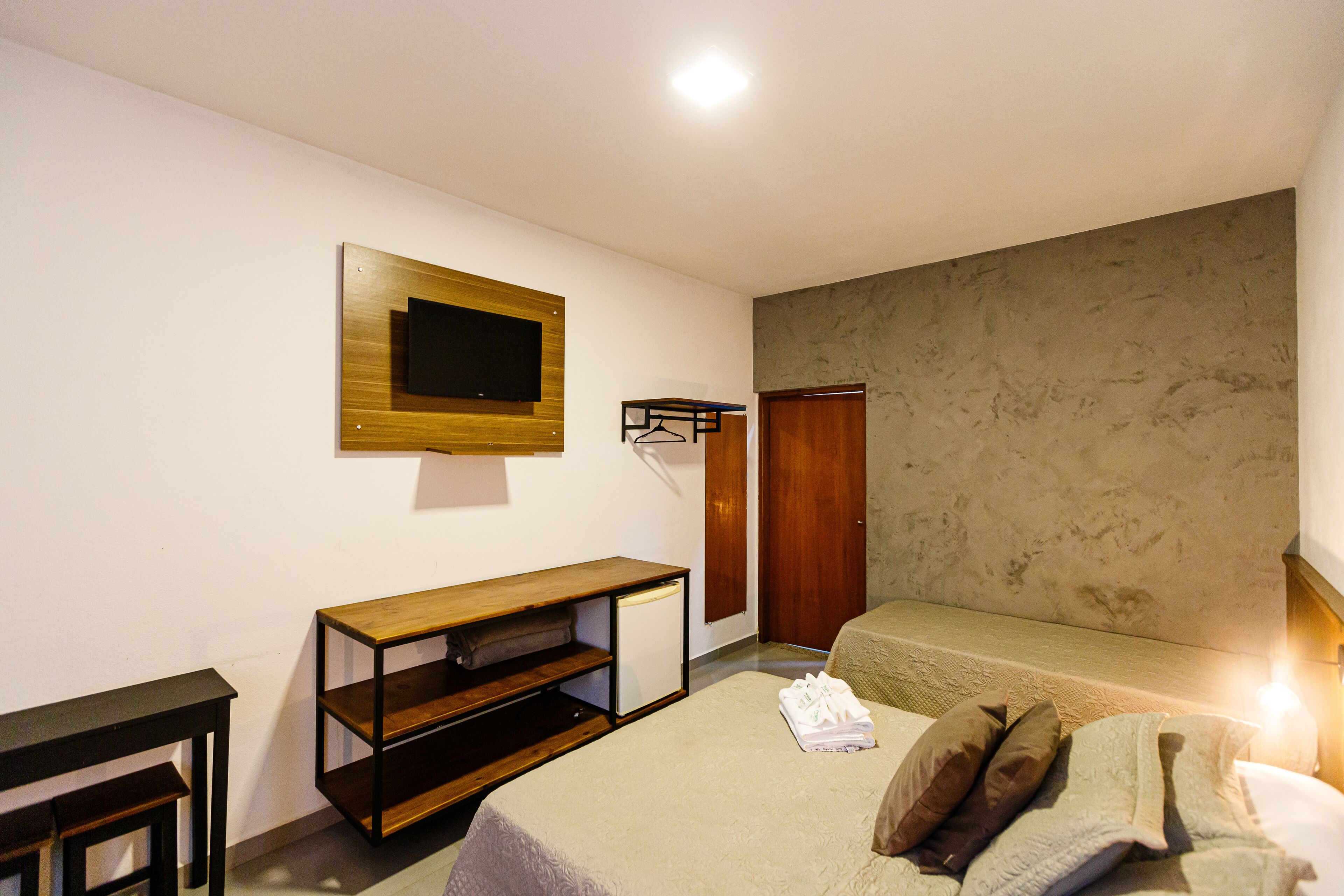 A bedroom with a bed, a TV mounted on the wall, a wooden shelf, and a wardrobe.