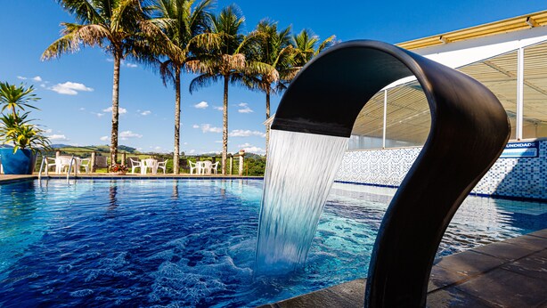 Une piscine agrémentée d’un élément décoratif aquatique, entourée de palmiers et dotée d’une terrasse carrelée.