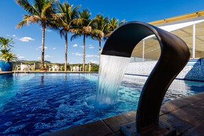 Une piscine agrémentée d’un élément décoratif aquatique, entourée de palmiers et dotée d’une terrasse carrelée.
