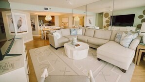 A modern living room with a large sectional sofa, a round coffee table, and a flat-screen TV. - 🌞CBC 2-11B | Gulf-view 2BR/2BA condo on Clearwater Beach with pool & tennis! (Clearwater Beach)