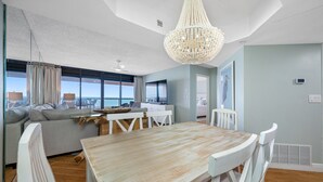 A modern living room with a dining area, large windows, and a view of the ocean. - 🌞CBC 2-11B | Gulf-view 2BR/2BA condo on Clearwater Beach with pool & tennis! (Clearwater Beach)