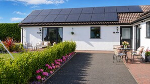 A single-story building with a solar panel roof, a garden with pink flowers, and outdoor seating. - Lodge 1 - Lytton Tree Lodge - Reydon (Reydon)