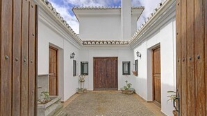 Un patio con una puerta central, flanqueado por dos puertas de madera, y un piso de baldosas.