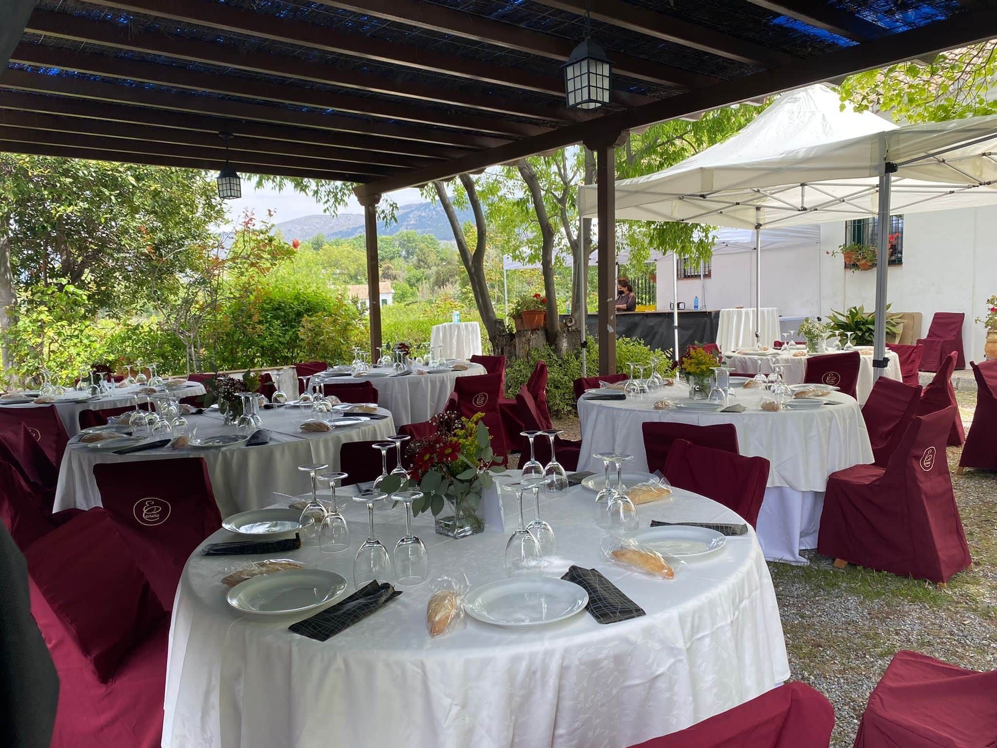 An outdoor dining area with round tables covered in white tablecloths, red chairs, and glassware.