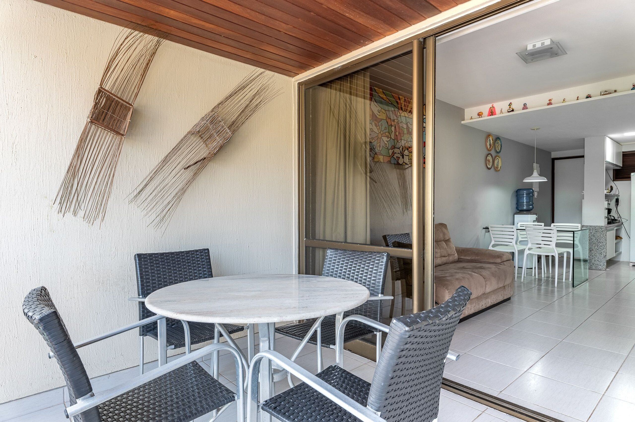 Un espace repas extérieur moderne, doté d’une table ronde et de chaises, d’un canapé et d’une porte-fenêtre coulissante donnant sur un espace intérieur.
