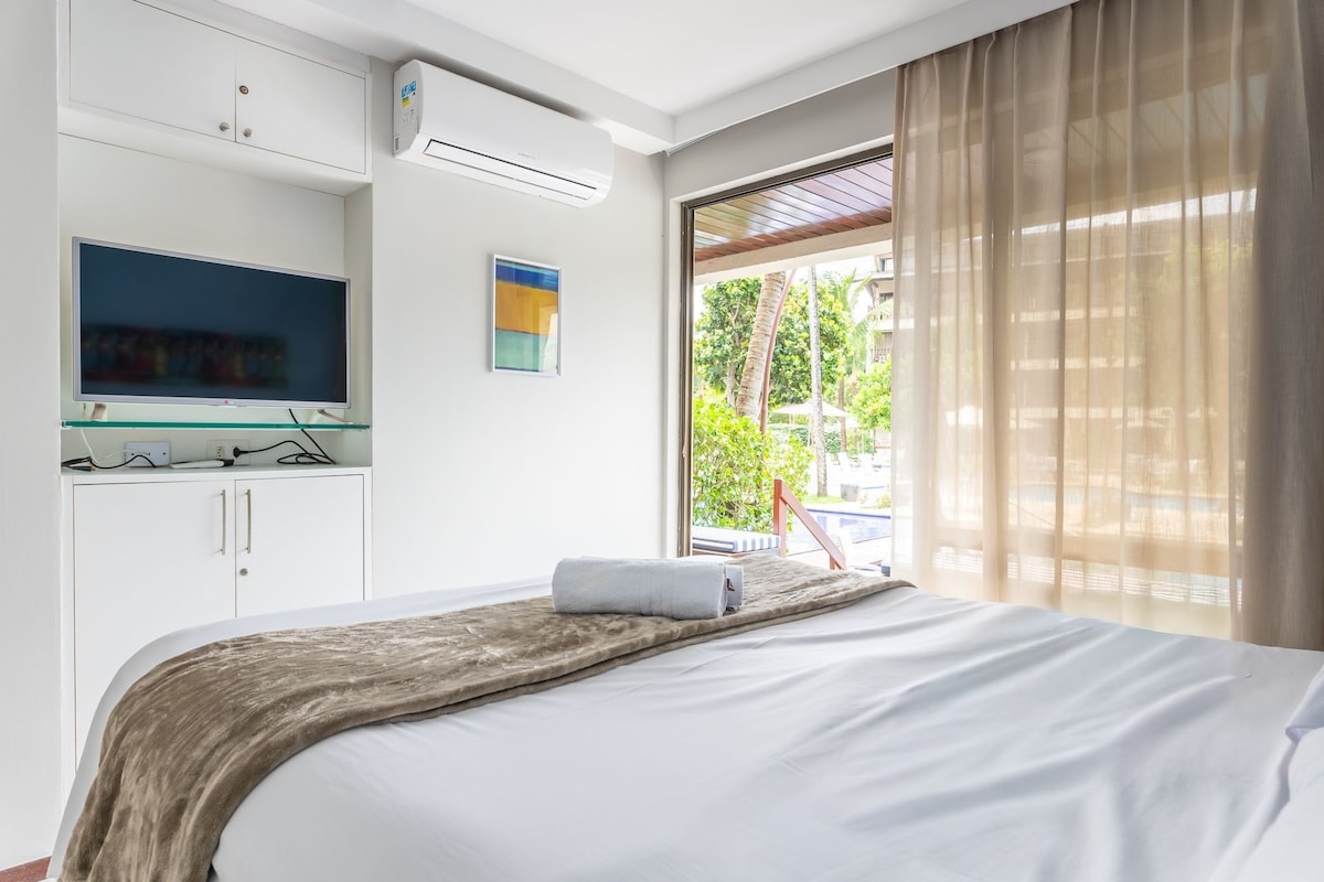 Ein Hotelzimmer mit einem Bett, einem Fernseher auf einer Glasablage, einer Klimaanlage und einem Fenster mit Vorhängen.