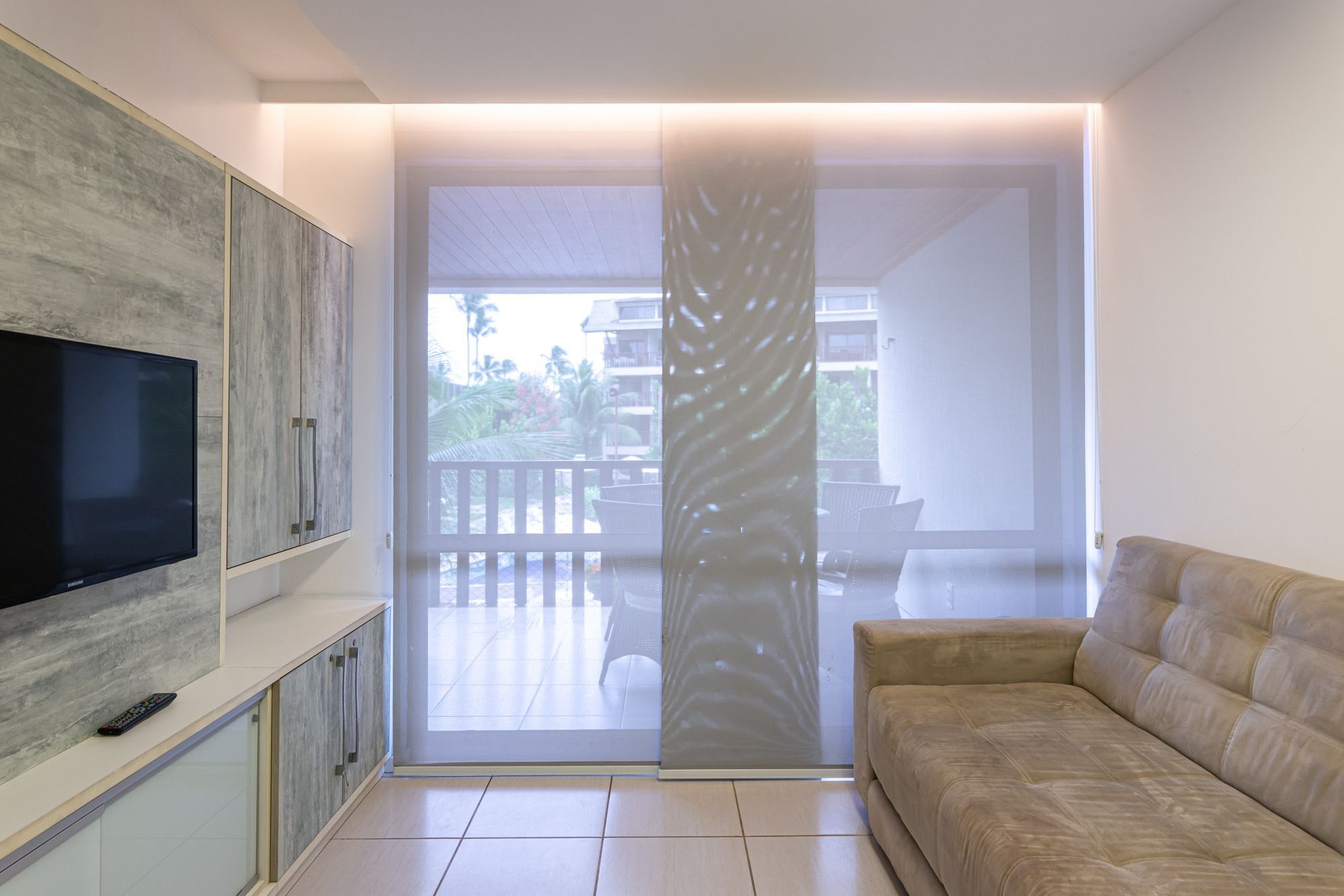 A modern living room with a flat-screen TV, a sofa, and a sliding glass door leading to an outdoor balcony.