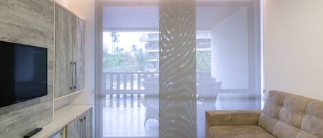 A modern living room with a flat-screen TV, a sofa, and a sliding glass door leading to an outdoor balcony.