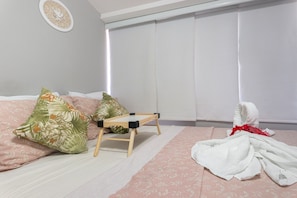Un dormitorio con cama, almohadas, una silla de madera y una ventana con persianas.