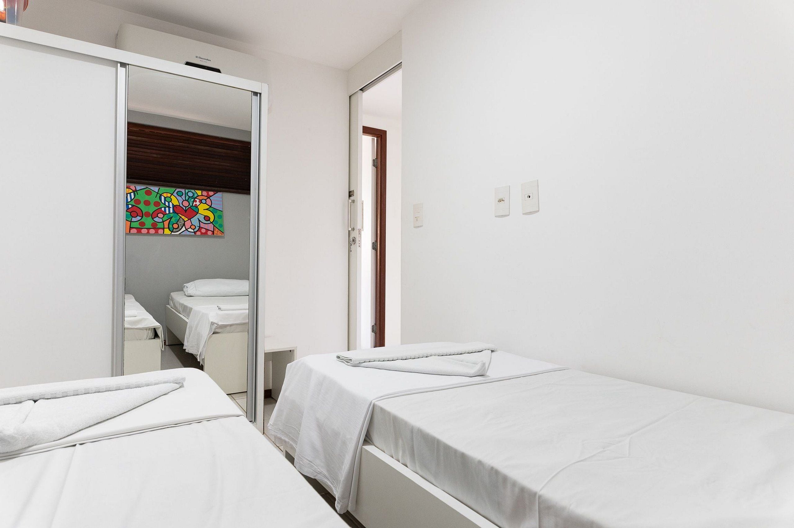 Een hotelkamer met twee eenpersoonsbedden, een garderobe, een spiegel en een deur naar een badkamer.
