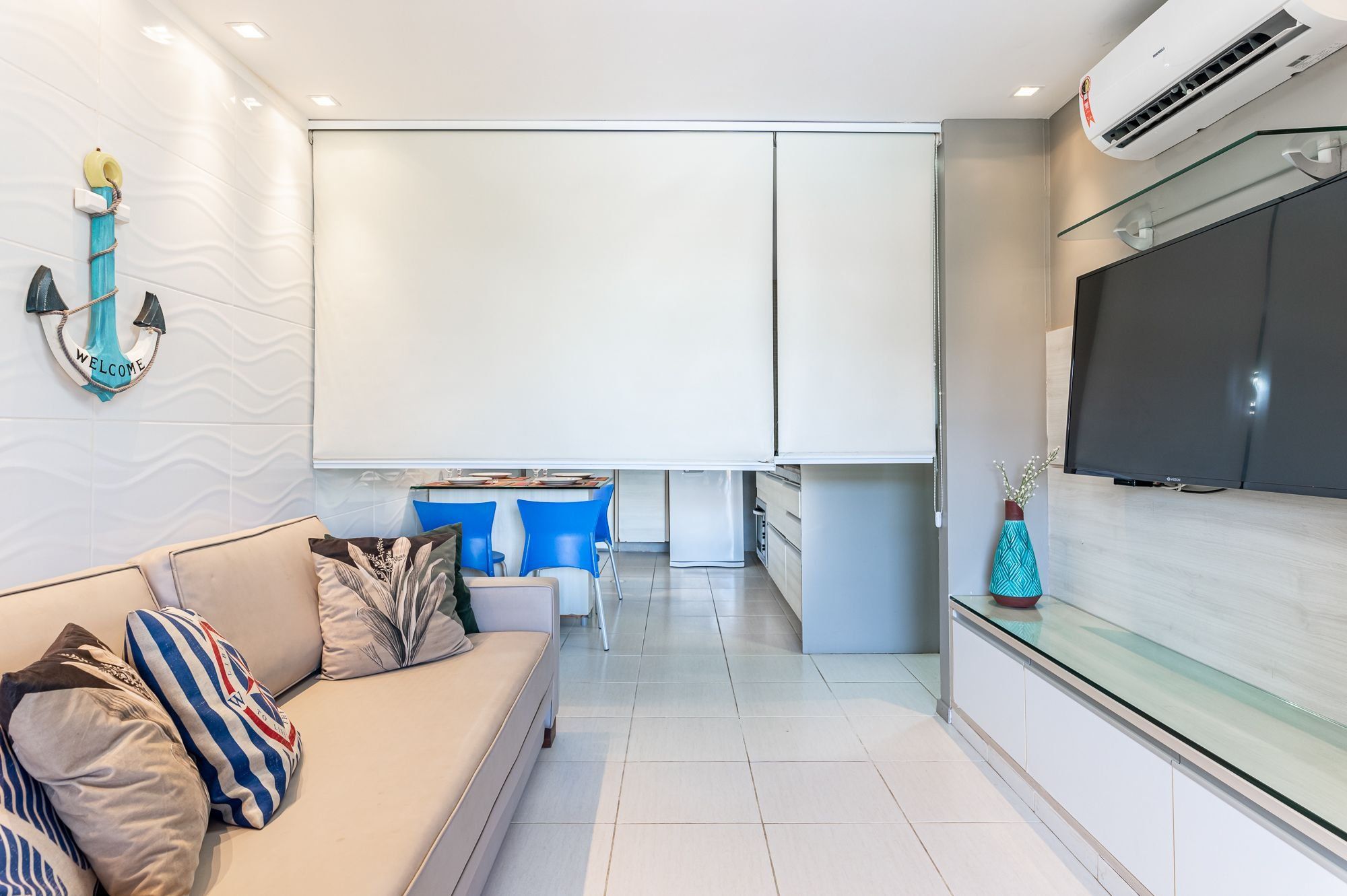 Ein modernes Wohnzimmer mit Sofa, Fernseher und Küchenbereich mit blauen Stühlen.