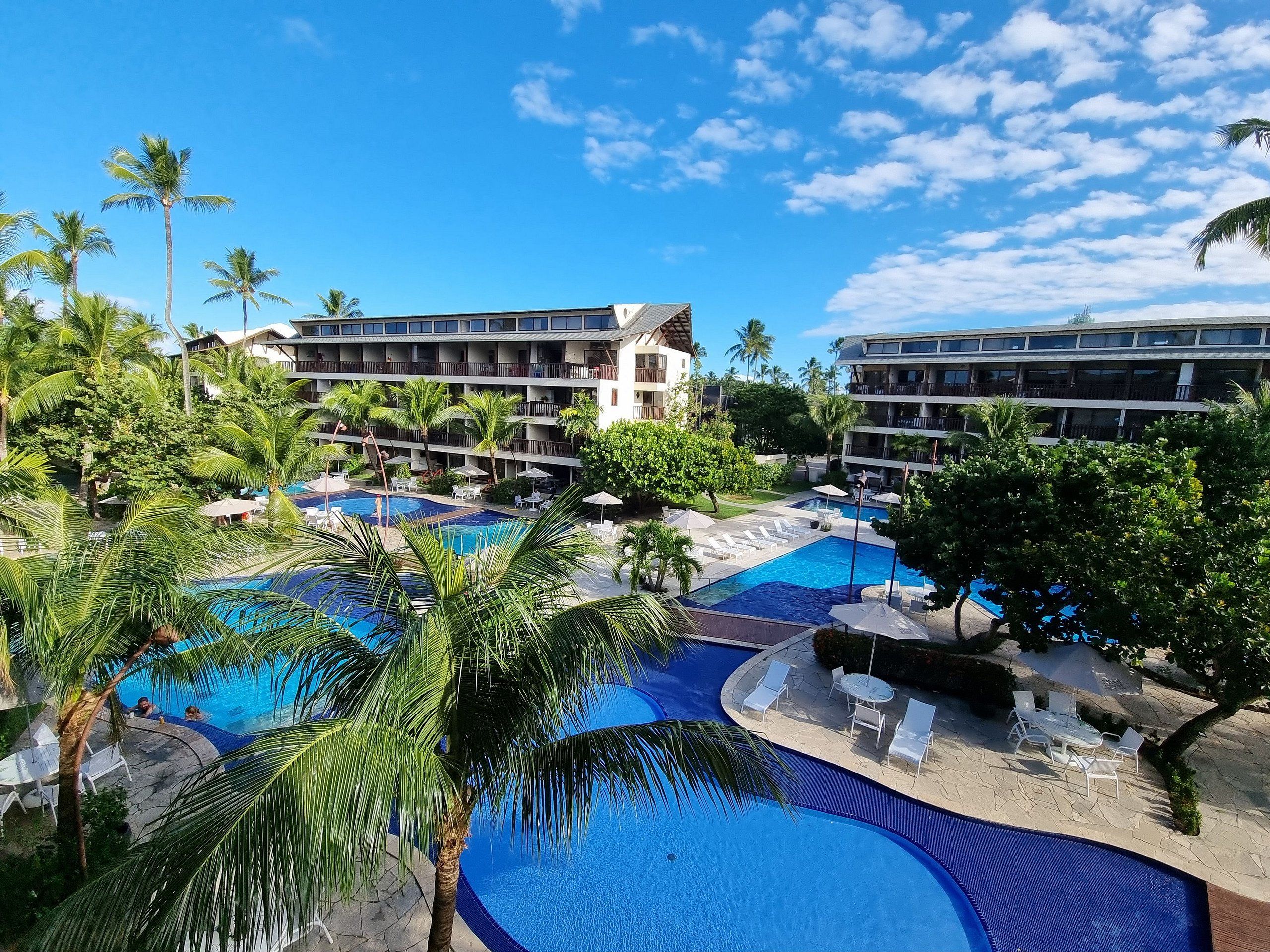 A resort with multiple swimming pools, palm trees, and a multi-story building with balconies.