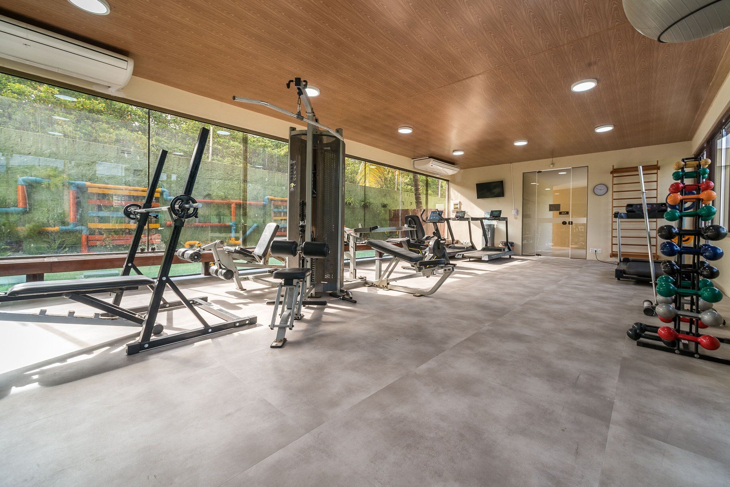 Une salle de sport équipée de divers appareils d’exercice, dotée de grandes fenêtres et offrant une vue sur un espace extérieur.