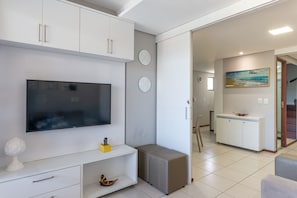 Una sala moderna con un televisor de pantalla plana, un mueble blanco, un taburete pequeño y un cuadro en la pared.