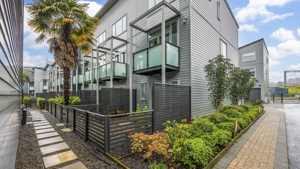 Un edificio moderno con un balcone, una palma e un'area giardino.