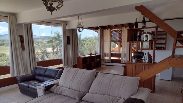 Amplia sala de estar con sofá, escalera de madera y vistas al exterior.