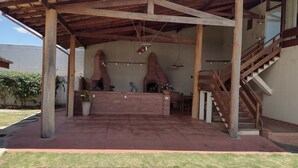 Un patio al aire libre con chimenea de ladrillo, pérgola de madera y una escalera que lleva a un nivel superior.