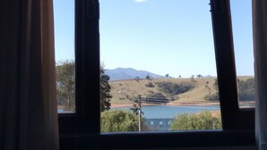 Una ventana con vistas a un paisaje que incluye colinas, una masa de agua y un cielo despejado.
