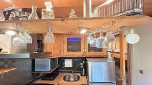 Cocina compacta con armarios de madera, un refrigerador de acero inoxidable y cristalería colgante.