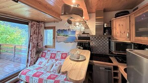 Cocina compacta con armarios de madera, comedor con mesa y sillas, y vista al exterior a través de una ventana.