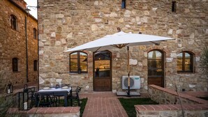 A stone building with a patio area featuring a table and chairs, an outdoor fan, and a large umbrella.