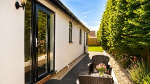 A covered patio with outdoor seating, a glass door entrance, and a well-maintained garden.