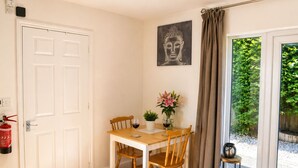 A room with a white door, a table with chairs, a Buddha painting, a window with curtains, and a fire extinguisher.