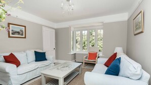 A spacious living room with two white sofas, a coffee table, and a window with a view of greenery. - Wonderful thatched cottage in The New Forest (Minstead)