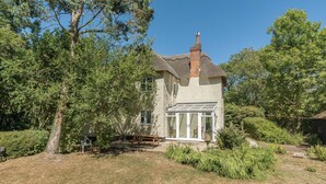A house with a large front porch, a chimney, and a garden with trees and shrubs. - Wonderful thatched cottage in The New Forest (Minstead)
