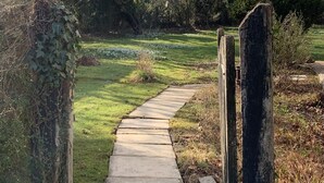 A concrete pathway leading through a garden with a wooden gate. - Wonderful thatched cottage in The New Forest (Minstead)