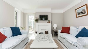 A modern living room with white sofas, a central coffee table, a fireplace, and a television mounted above it. - Wonderful thatched cottage in The New Forest (Minstead)